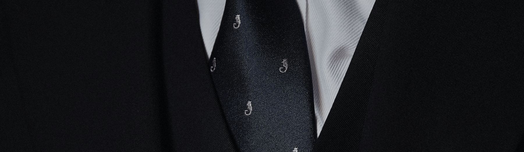 Close detail of a dark tailored jacket, shirt and patterned tie