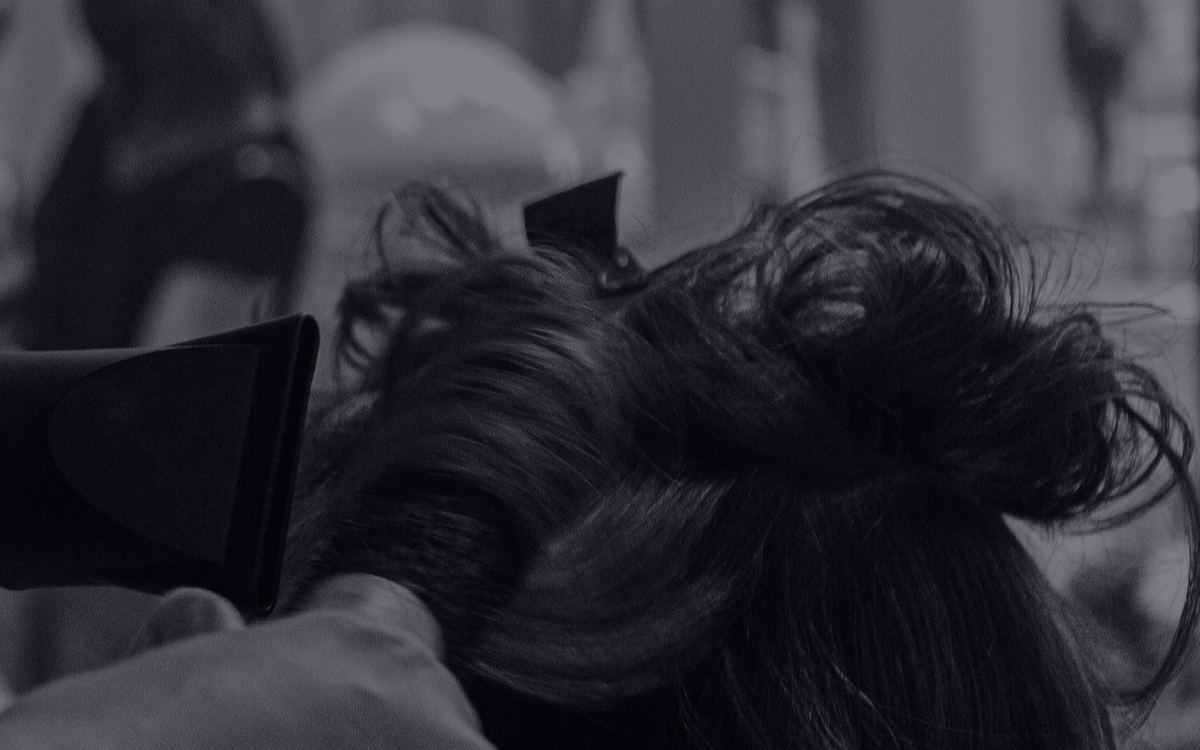 Stylist blow-drying a client's hair, black-and-white salon scene