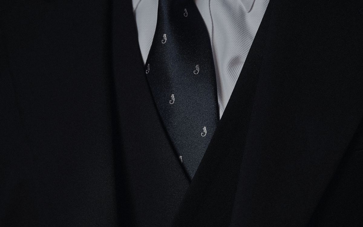 Close detail of a dark tailored jacket, shirt and patterned tie